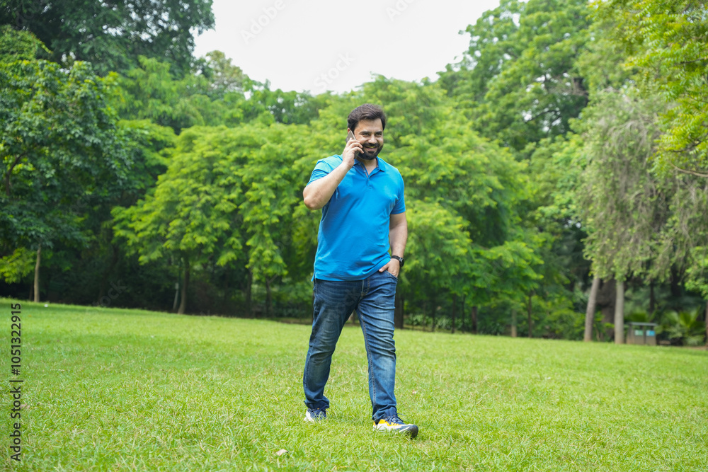 Young happy indian man talking on the phone outdoor at summer park while walking. Wireless Technology. Communication.