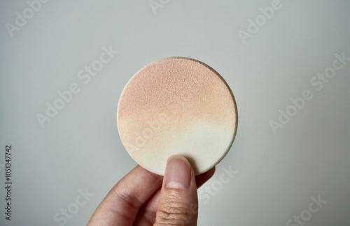 Hand holding round compact powder cushion object isolated on horizontal ratio plain wall background. photo