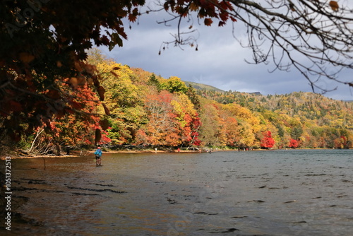 紅葉の湖畔で釣りをする人