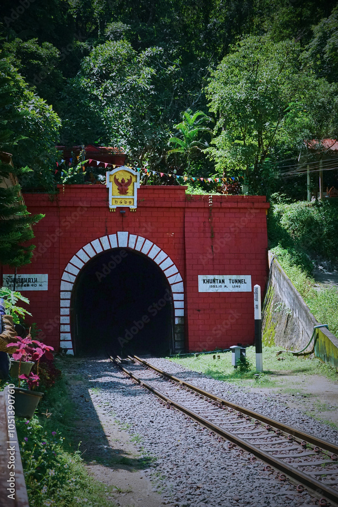 Obraz premium Entrance of a railway tunnel with red brick facade surrounded by lush greenery.