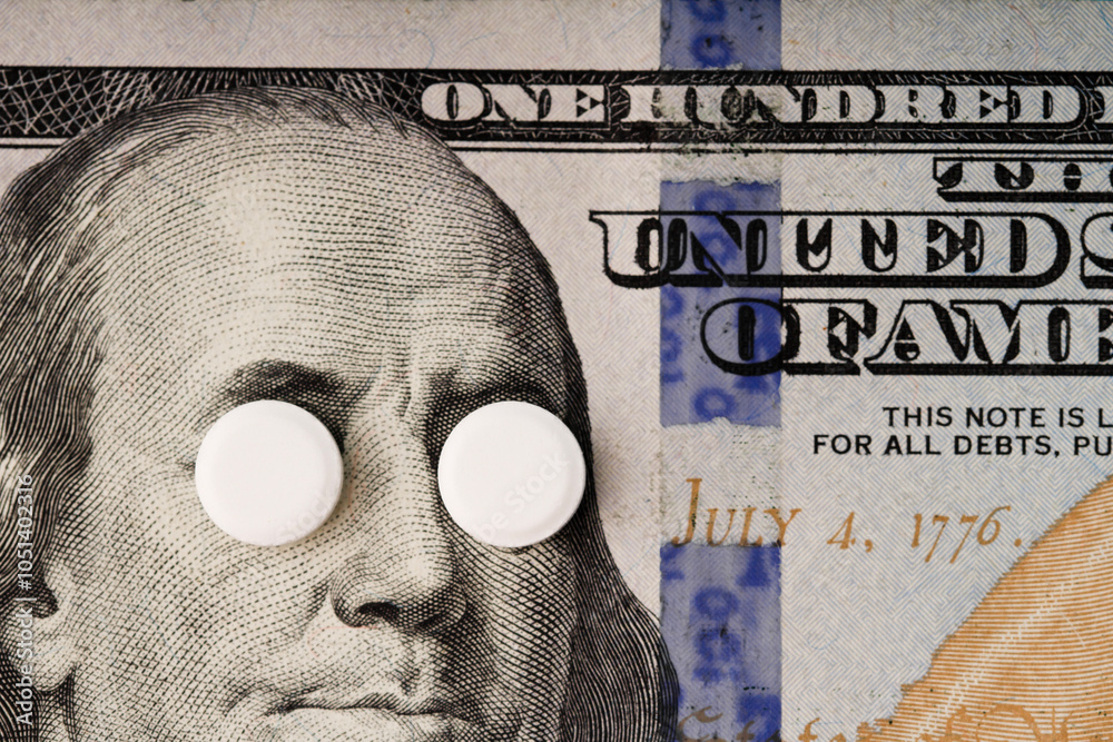High cost of medications concept . White pills covers Franklin's eyes on a banknote of 100 US dollars.