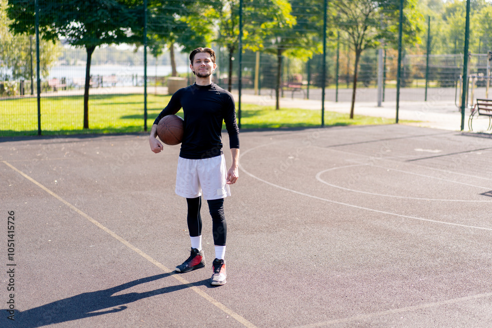 Obraz premium a sports ground basketball field active recreation guy in white shorts and black t-shirt stands with ball in hands posing in front of camera