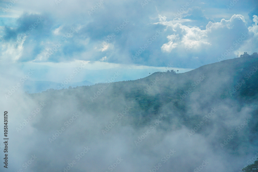 Obraz premium A serene landscape with hills shrouded in mist under a cloudy sky.