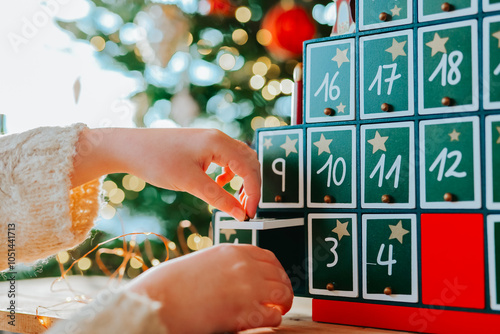 Child opens Christmas advent calendar doors on christmas tree background.Gifts and surprises.Christmas Tree Advent Calendar and a child in a bright, cozy room