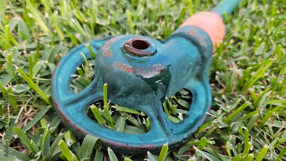 Close-up of a garden sprinkler and house with rust and water, sitting on a bright green grass lawn Close-up of a garden sprinkler and house with rust and water, sitting on a bright green grass lawn