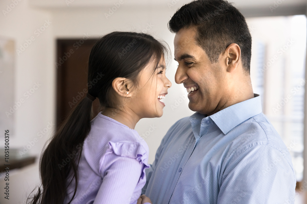 Cheerful loving Indian dad cuddling pretty daughter kid, laughing, hugging child with noses touch, enjoying parenthood, closeness, trust, family relationship. Side view candid shot Cheerful loving Indian dad cuddling pretty daughter kid, laughing, hugging child with noses touch, enjoying parenthood, closeness, trust, family relationship. Side view candid shot