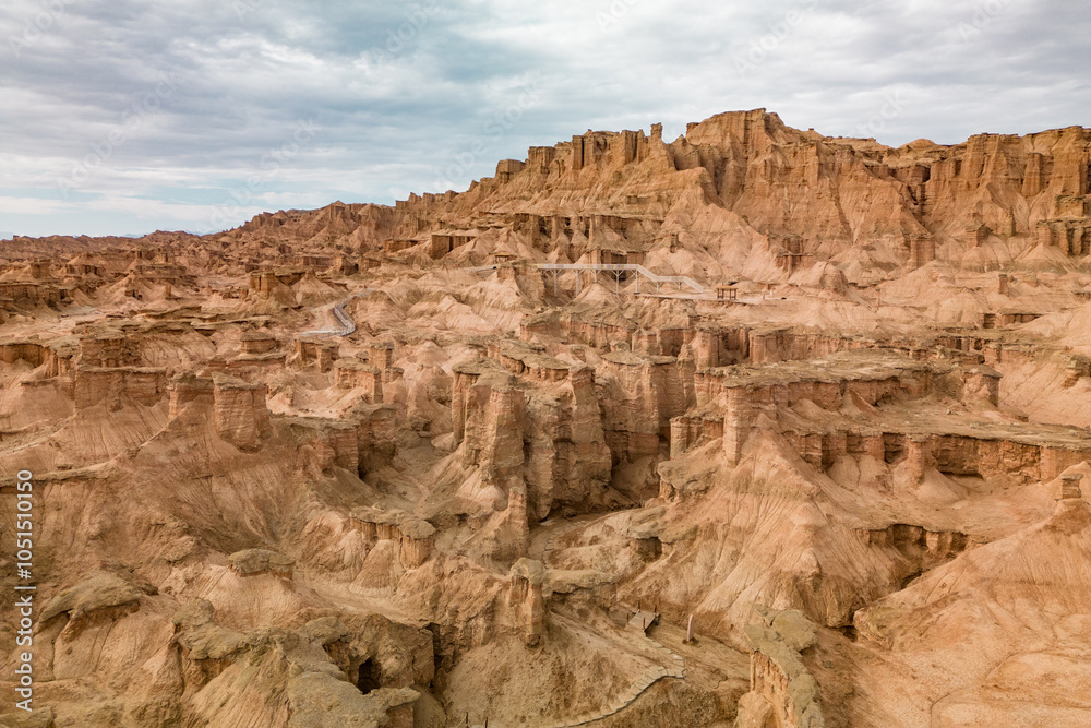 A breathtaking aerial view of a rugged desert canyon landscape at golden hour, showcasing dramatic rock formations, sandy terrain, and a winding road under a clear sky A breathtaking aerial view of a rugged desert canyon landscape at golden hour, showcasing dramatic rock formations, sandy terrain, and a winding road under a clear sky