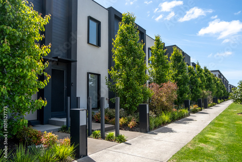 Fototapeta Naklejka Na Ścianę i Meble -  Sleek urban row of modern townhouses with contemporary landscaping and tree-lined pedestrian walkways. Residential street view in an Australian suburban neighborhood featuring small front yards.