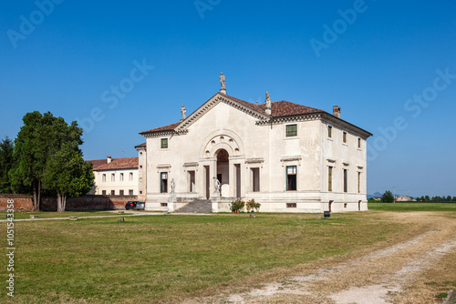 This grand villa showcases Palladian architecture with a stately colonnade, sculpted statues on the roofline, and arched entrances. A serene garden and central well enhance the classical ambiance. photo