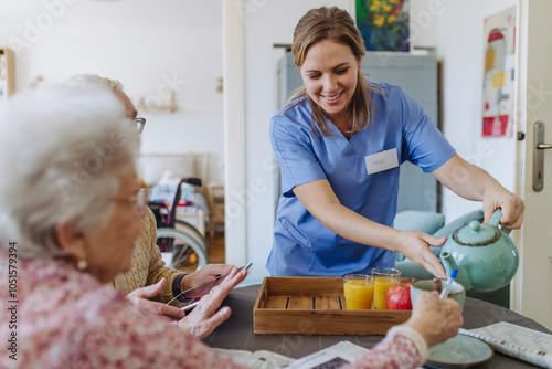 Smiling healthcare worker serving tea to senior couple photo