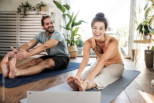 Happy couple watching tutorial and doing stretching exercise together on mats at home