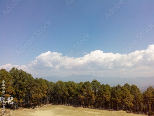 A view of forests on hills, having a ground in the middle and surrounded by trees along with the blue sky complimenting the landscape in Dharamshala, Himachal Pradesh, India, Asia photo