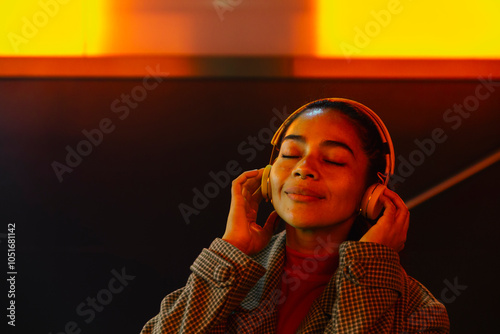 Woman enjoying music with eyes closed on headphones at illuminated subway station photo