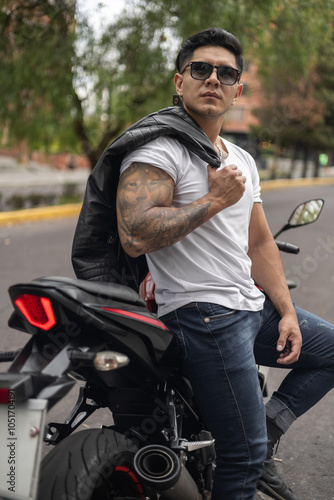 Attractive young man with short hair, athletic body sitting on his motorcycle wearing glasses and holding his leather jacket, male model lifestyle photo