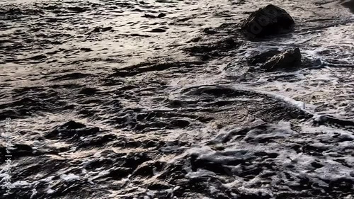 Waves gently lap at shore during stunning sunset over ocean. Golden sunlight reflects off waves as they roll onto shore, creating tranquil atmosphere at sunset by sea. Montenegro summer, Canj photo