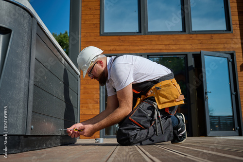 Plumber installing hot tub. Spa technician performing hot tub. Bathtub plumbing. Plumber fixing spa zone. Professional in uniform inspects and prepares a hot tub located on a stylish outdoor patio.
