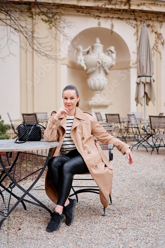 Photography Young prety woman wearing coat is sitting in outdoor cafe in Wien