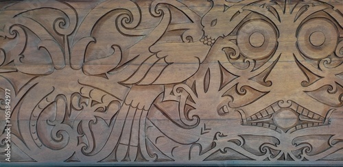 Carvings on a wooden wall featuring traditional Dayak motifs, including the hornbill bird, a dragon-like creature, and a broad face with large eyes.