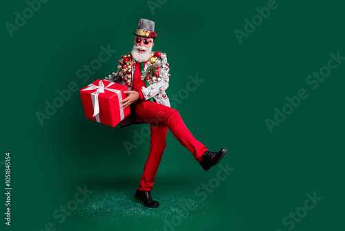 Full body portrait of eccentric grandfather giftbox xmas tree toys blazer red pants empty space isolated on dark green color background