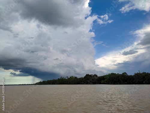 A view of thick clouds pouring heavy rain over the land and river below, creating a misty atmosphere.