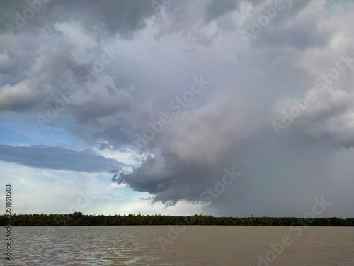 A view of thick clouds pouring heavy rain over the land and river below, creating a misty atmosphere.