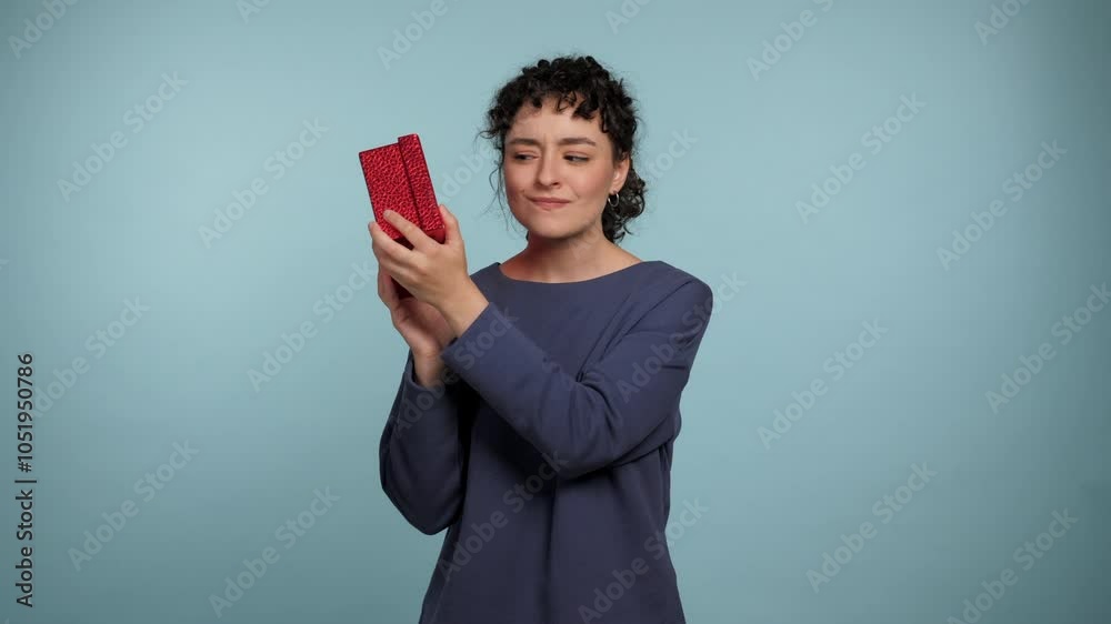 Beautiful smiling curly woman shaking wrapped present red box near ear being interested what inside. Positive female wearing blue sweater with gift in his hands on isolated light blue background Beautiful smiling curly woman shaking wrapped present red box near ear being interested what inside. Positive female wearing blue sweater with gift in his hands on isolated light blue background