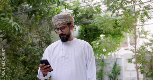 Omani man wearing omani traditional dishdasha and Musaar is looking at his cell phone