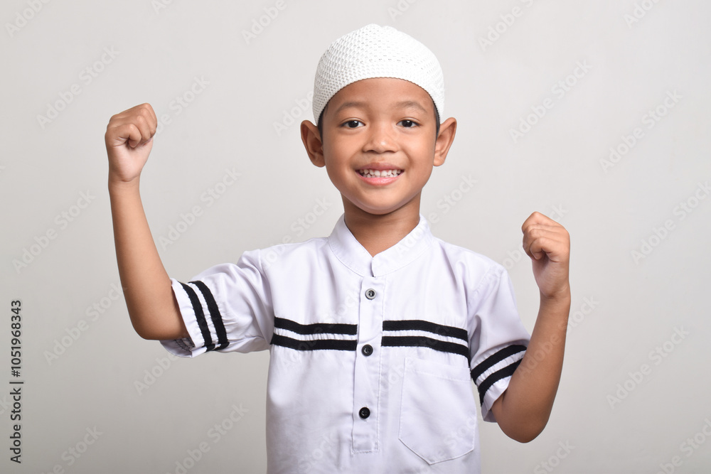 A happy and excited Muslim Asian boy with raised hands isolated on white background