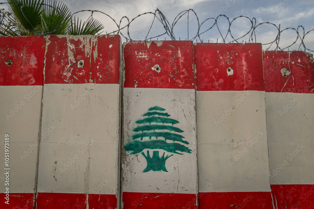 Fototapeta premium The Lebanon flag image on the concrete fence with barbed wire, at conflict region of Middle East, in Lebanese city of Beirut. 