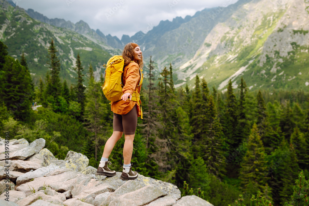 Naklejka premium Happy woman tourist with backpack enjoys the beautiful scenery of the majestic mountains. Adventure, travel concept.