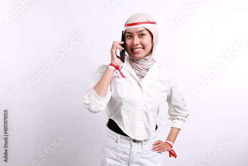 Smiling happy young Asian Muslim woman wearing a hijab talking on mobile phone and looking at camera isolated over white background. Celebrate Indonesian independence day on 17 August photo