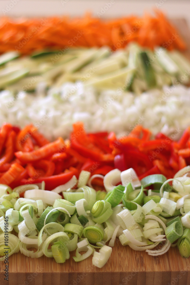 Chopped leek, red pepper, onion, zucchini and carrot on the chopping board. Cooking and meal prepping at home. Selective focus.