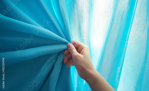 Hand Pulling Open Blue Curtain in Sunlight: A hand pulling aside a blue curtain, letting warm sunlight into the room, symbolizing freshness and a new start. photo