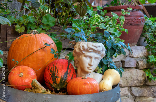 Cozy outdoor autumn scene with lit pumpkins and with classical bust and blooming flowers. Rustic autumn decor. Classical meets country: Fall decor with roman bust and orange pumpkins photo