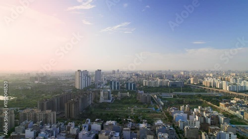 aerial drone shot of gurgoan cityscape with small builder floor houses in foreground with multi storey skyscrapers with apartments, offices in the distance shot at sunset