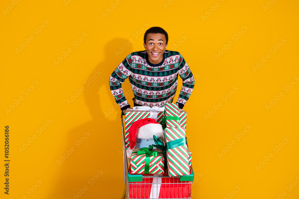Photo of funny young man excited push shopping cart gifts dressed ornament clothes christmas theme party on yellow color background Photo of funny young man excited push shopping cart gifts dressed ornament clothes christmas theme party on yellow color background