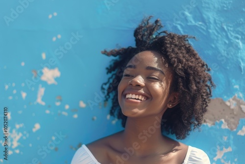 Portrait of happy young black woman laughing against blue wall