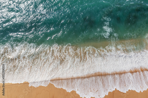 Azure ocean water and ocean foam covering beautiful long sandy beach, aerial drone view. Beautiful nature background.