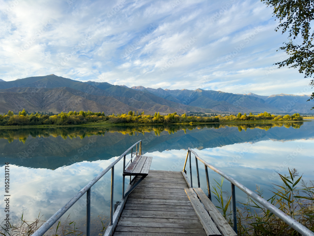 Fototapeta premium A wooden pier on Issyk-Kul lake with a view of the mountains. A beautiful spot for relaxation and enjoying the natural landscapes of Kyrgyzstan