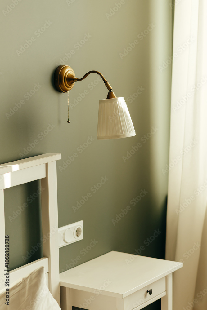 Wall mounted lamp in bedroom with white furniture. The wall is painted pistachio color.