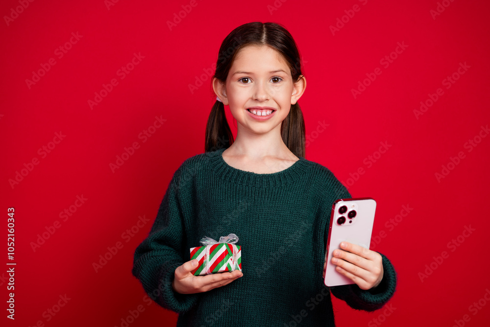 Photo portrait of pretty small girl hold gift device wear green christmas outfit theme party on red color background Photo portrait of pretty small girl hold gift device wear green christmas outfit theme party on red color background