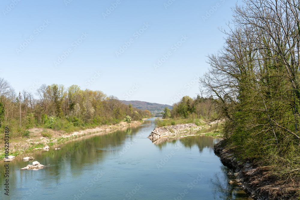 Obraz premium Beautiful rural landscape with river in a limestone bed, reflecting the trees on both sides, under a blue sky. Afternoon spring shot.