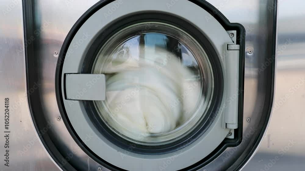 Machines à laver – Gros plan sur porte d'une machine à laver industrielle dans une laverie automatique publique avec une couette qui tourne dedans.