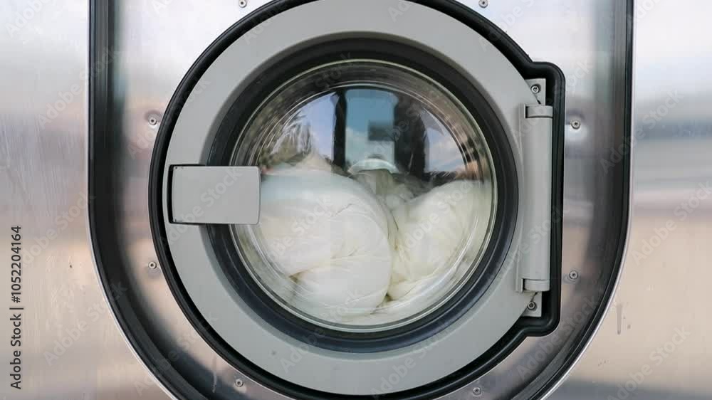 Machines à laver – Gros plan sur porte d'une machine à laver industrielle dans une laverie automatique publique avec une couette qui tourne dedans.