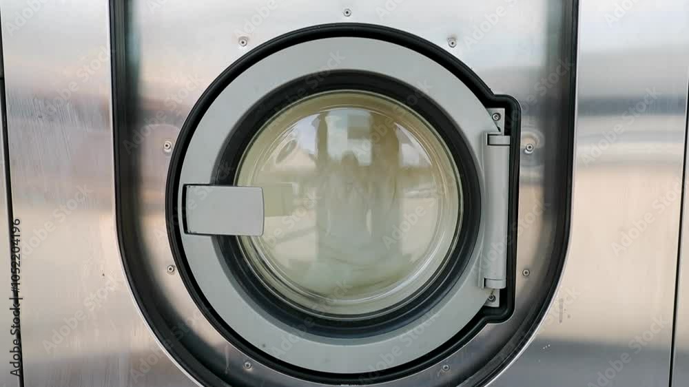 Machines à laver – Gros plan sur porte d'une machine à laver industrielle dans une laverie automatique publique avec une couette qui tourne dedans.