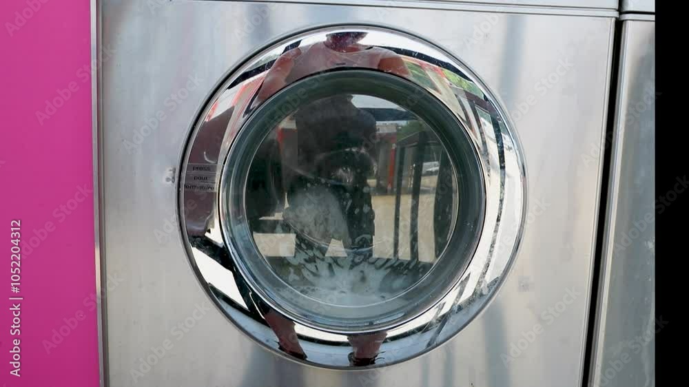 Machines à laver – Gros plan sur porte d'une machine à laver industrielle dans une laverie automatique publique avec une couette qui tourne dedans.