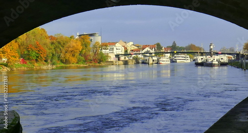 reizvoller Blick unter Brückenbogen der steinernen Brücke auf am Ufer liegende Ausflugsschiffe neben herbstlichen bunten Bäumen photo