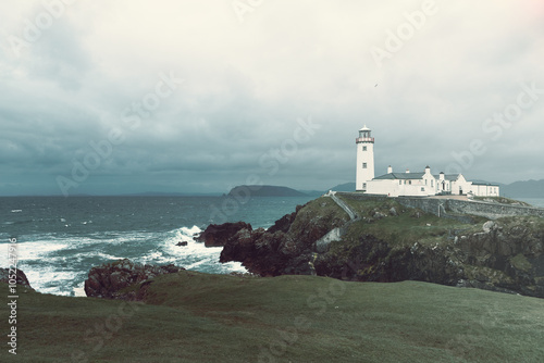Fanad Head Lighthouse stands resilient against the stormy Atlantic, with vintage tones adding a timeless quality. The dramatic waves and overcast sky enhance the coastal scene historic feel