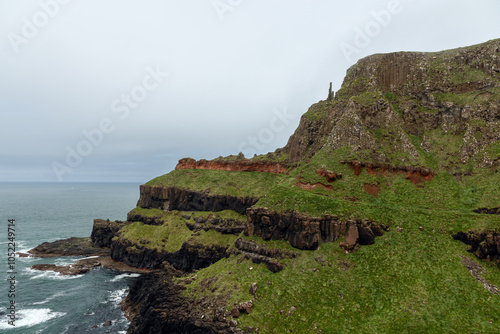 Coastal cliffs of Giant's Causeway featuring contrasting layers of black basalt and red rock. The textured landscape overlooks the turbulent Atlantic Ocean photo