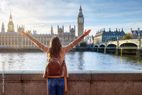 A happy tourist woman on a city sightseeing trip enjoys the view of the Westminster Palace and Big Ben tower in London, England